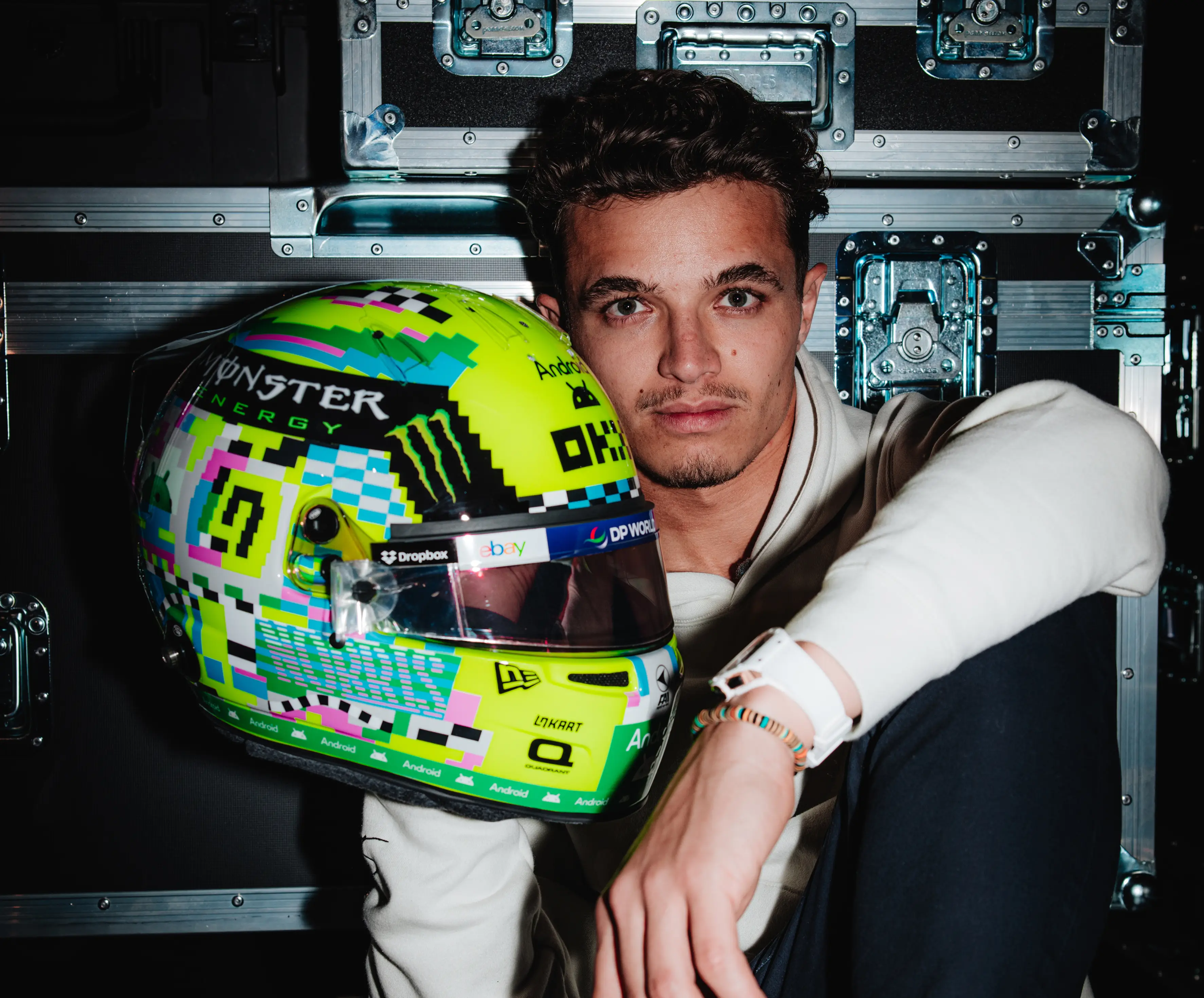Lando Norris hodling up a helmet with flight cases in the background