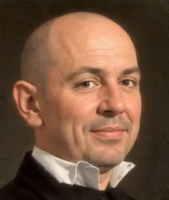 Portrait of a middle-aged bald man with a slight smile, wearing a black jacket over a white collared shirt.
