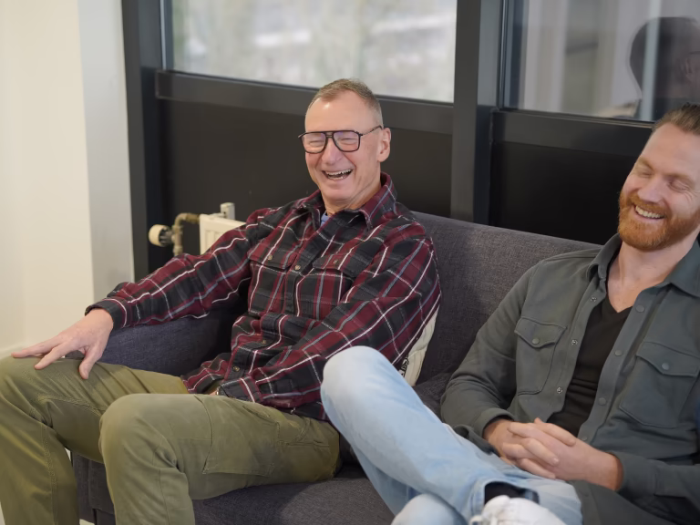 Twee mannen zitten op een bank en lachen ontspannen in een moderne kamer.