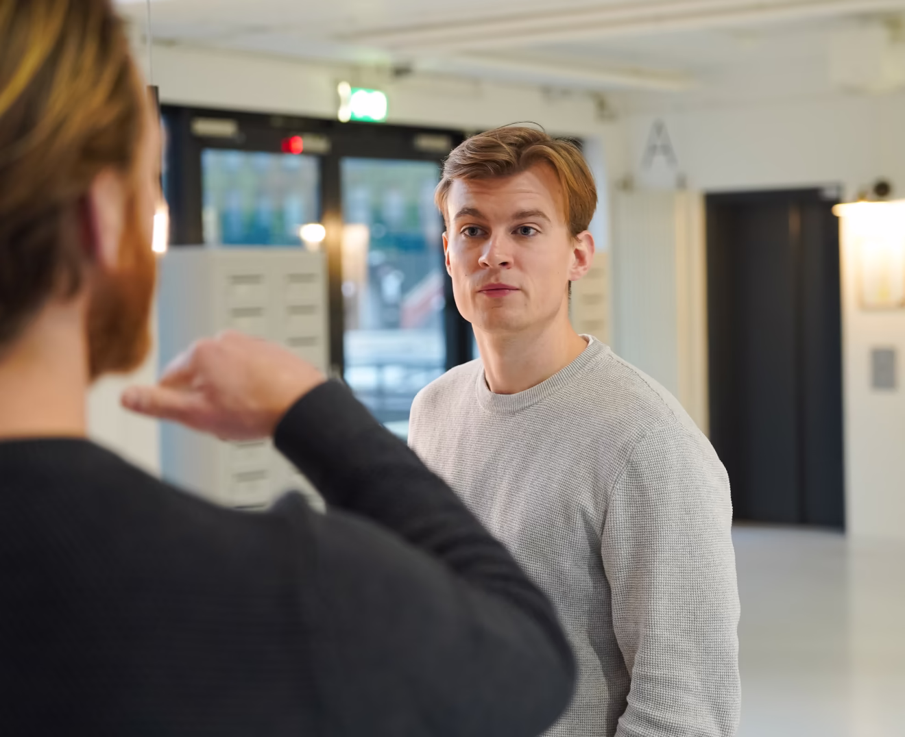 Twee jonge mannen die een serieus gesprek voeren in een moderne binnenruimte.