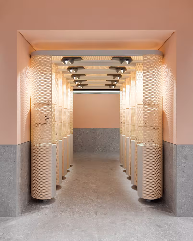 Minimalist hallway with gray stone floor, peach walls, and column-like light fixtures with perforated mesh panels.
