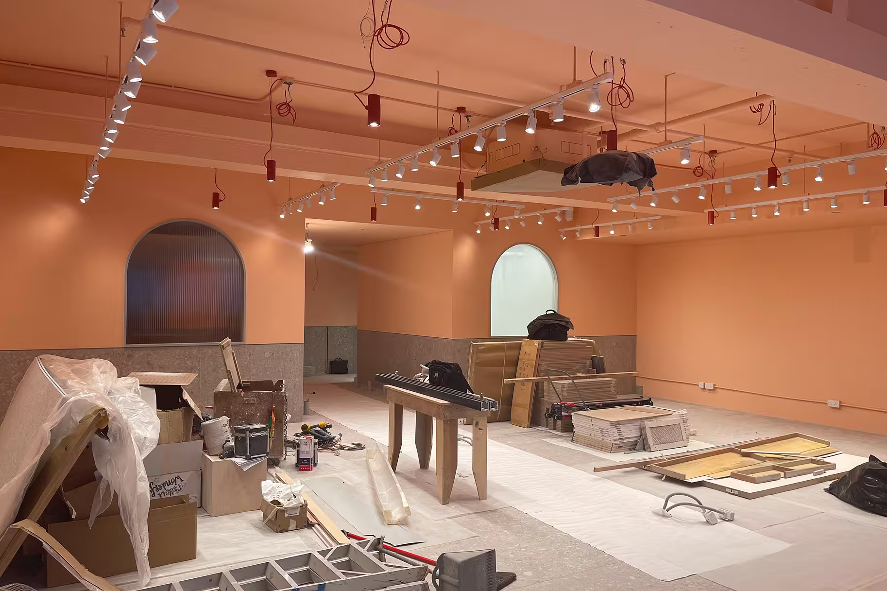 Interior under renovation with peach walls, arched windows, construction materials, and ceiling-mounted lights.