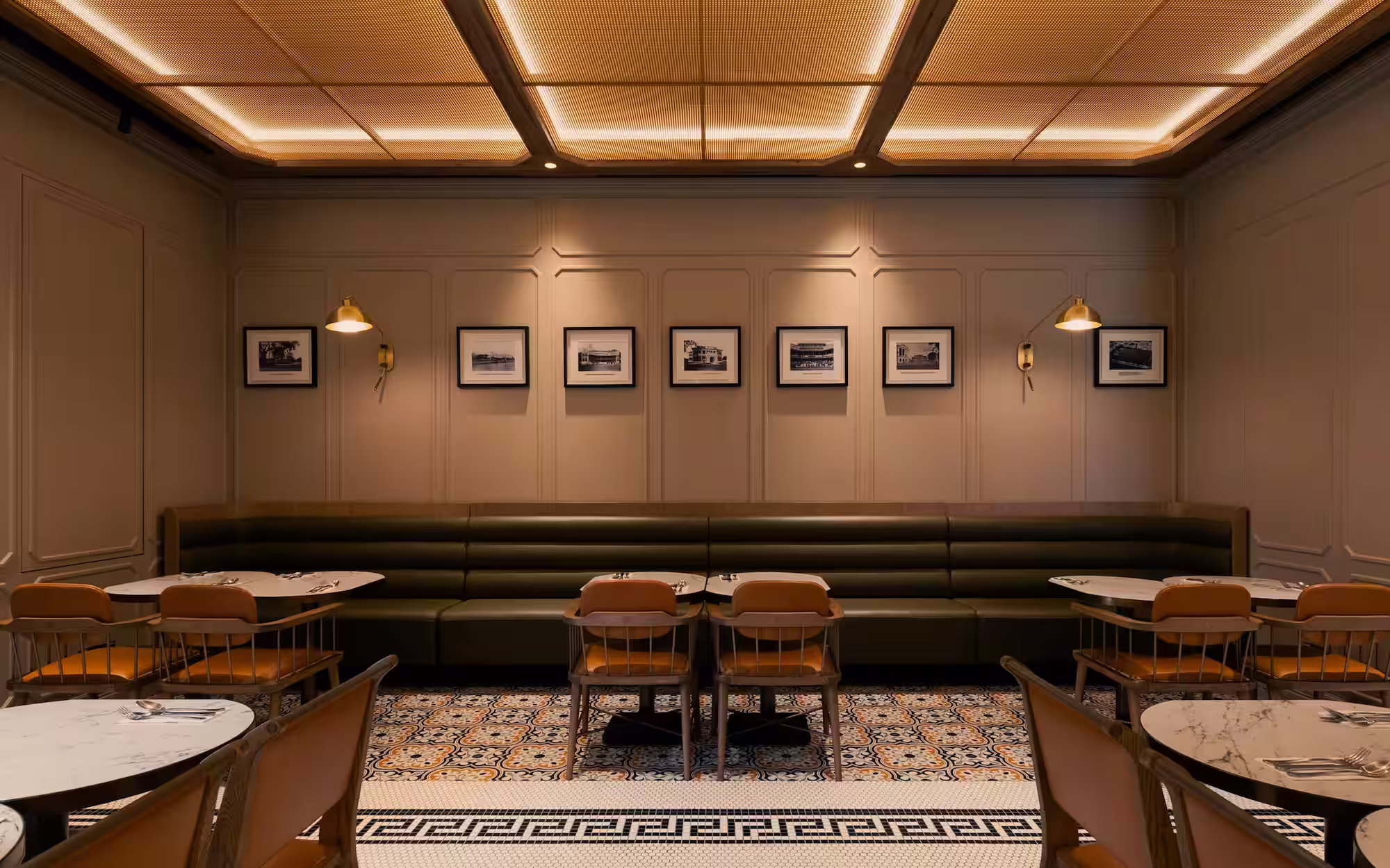 Elegant restaurant interior with green leather banquette, wooden chairs, marble tables, and patterned tile floor.