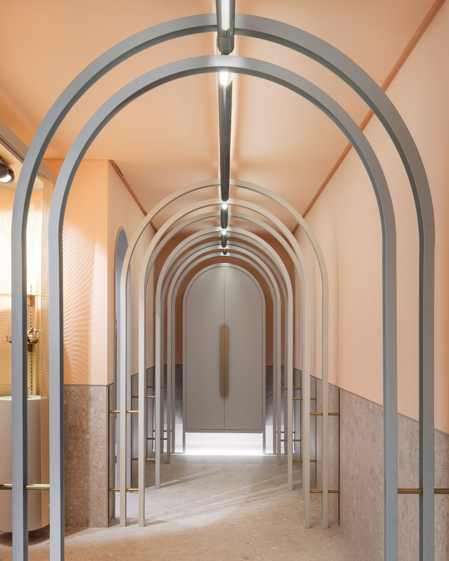 Minimalist corridor with multiple gray metal arch frames and soft peach walls leading to a closed door.