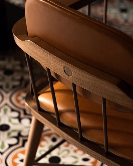 Close-up of a wooden chair with tan leather cushioning and vertical metal rods in a dimly lit room.