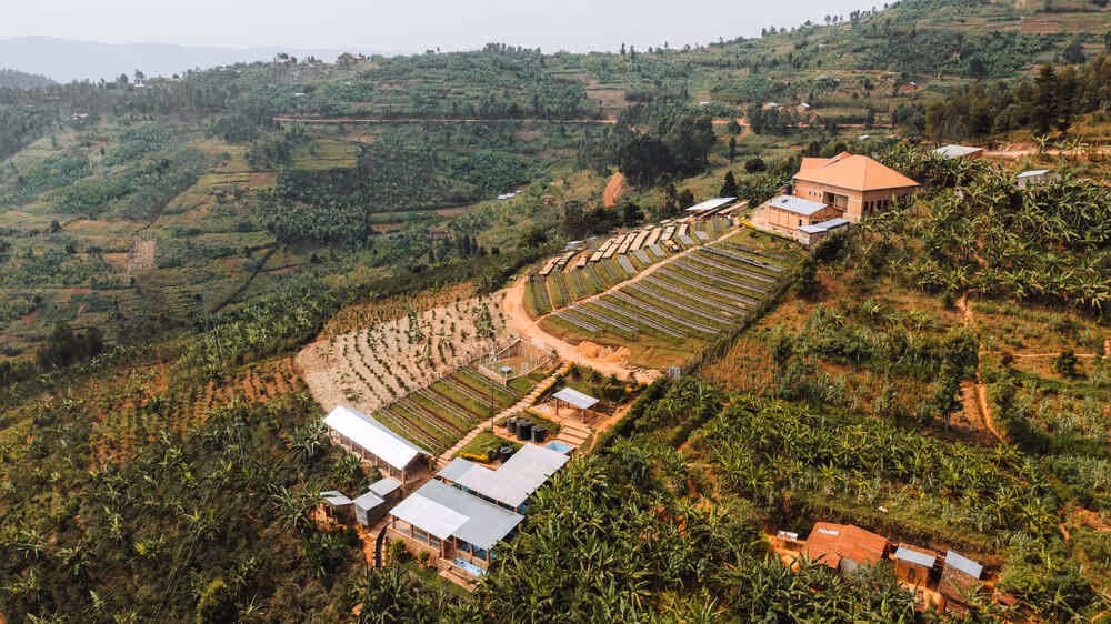 Aerial view of a terraced hillside farm with multiple greenhouses, agricultural plots, and buildings surrounded by lush vegetation.